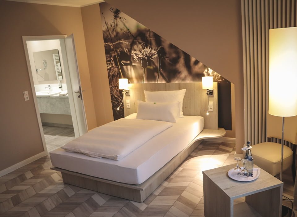 Einzelzimmer mit Bett, Stehlampe und Blick ins Bad